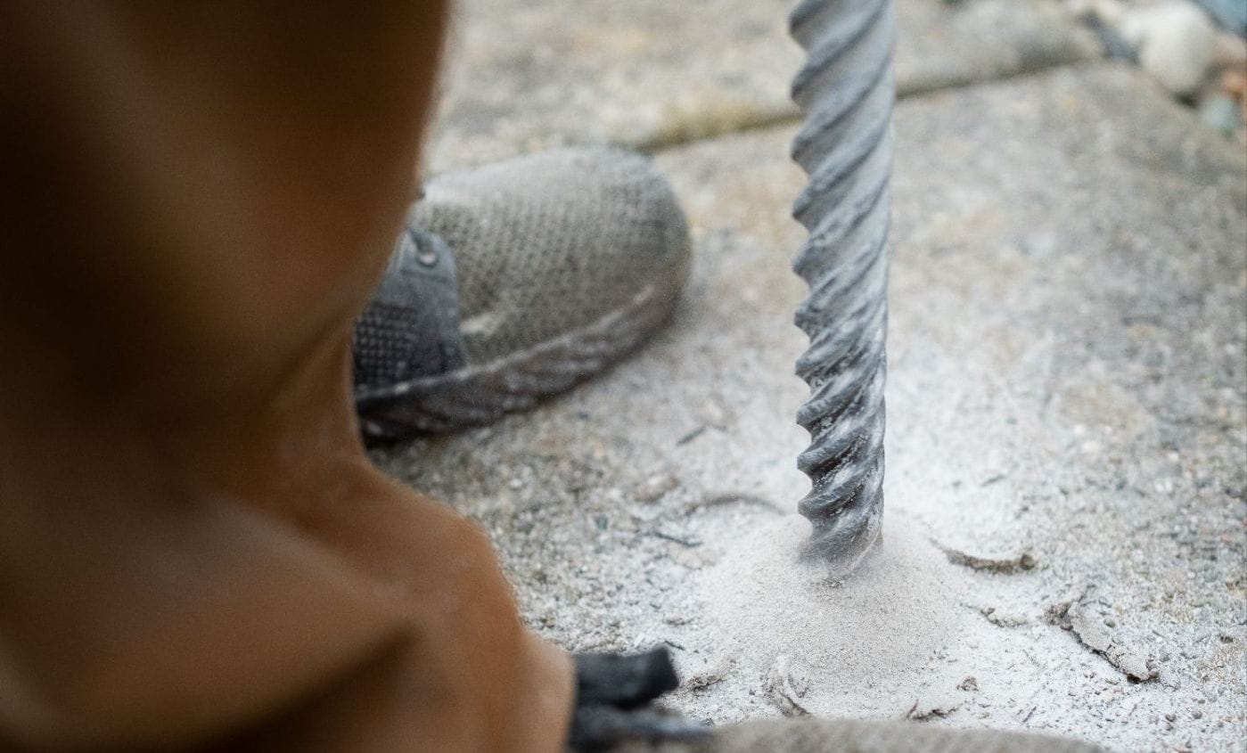 A worker drilling a small port through a sunken concrete slab