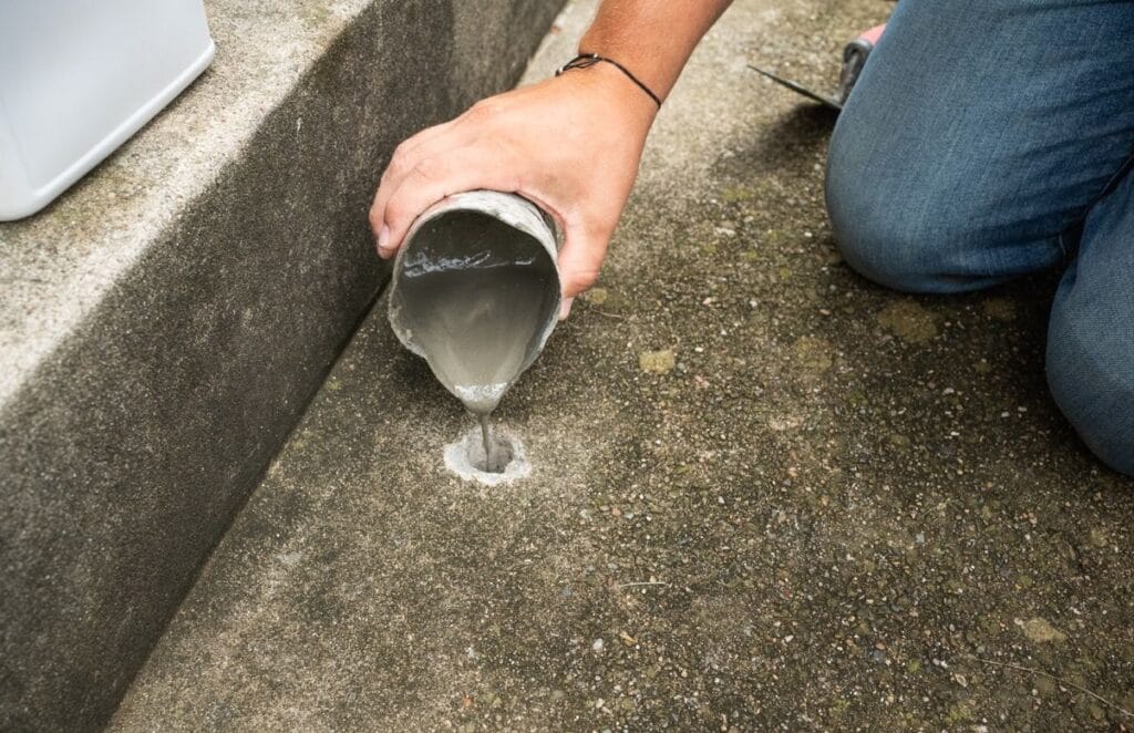 A dirt and mortar slurry being poured to fill the voids beneath a concrete slab