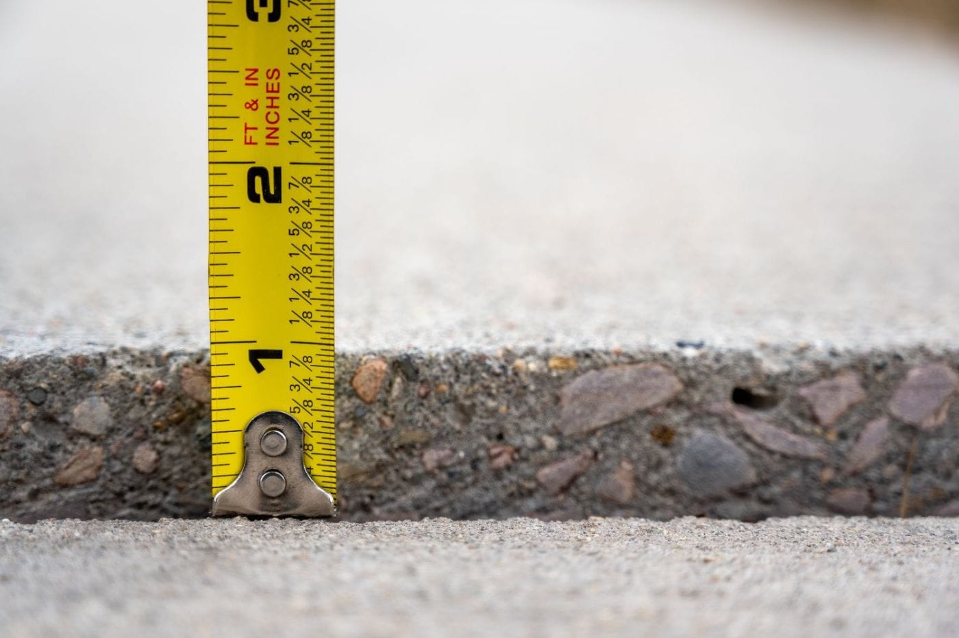 A tape measure showing how far one concrete slab has settled below the one beside it
